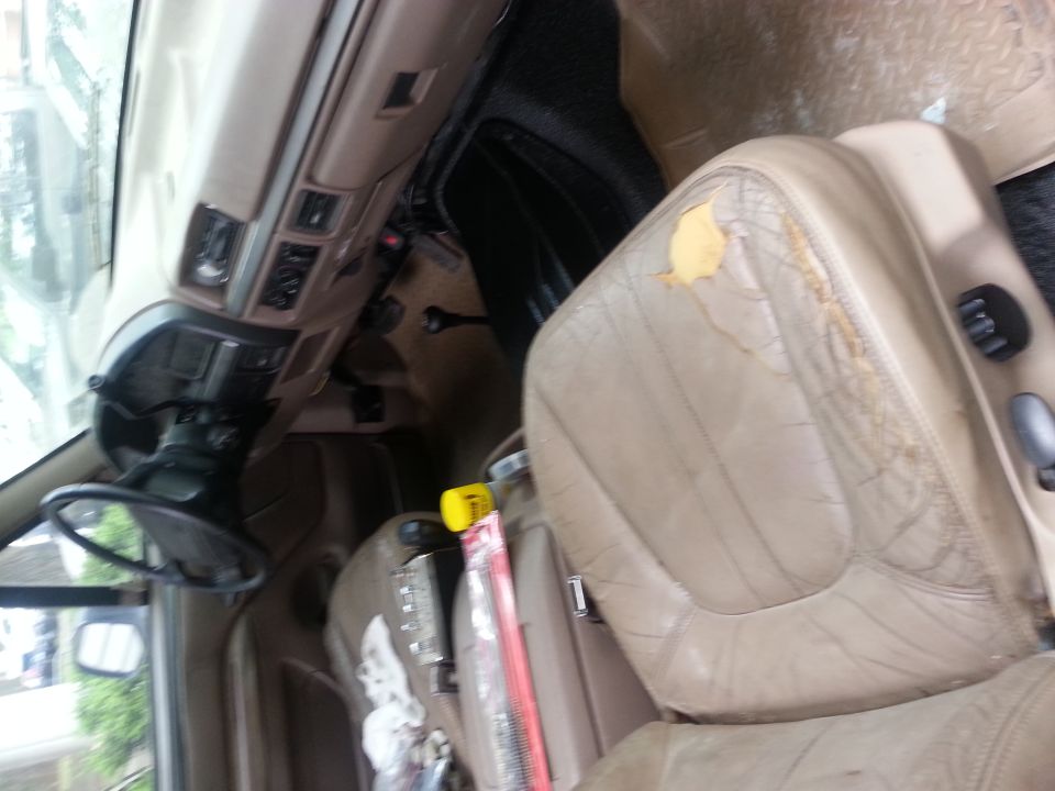 Interior of a vehicle showing a damaged tan leather driver's seat and dashboard.