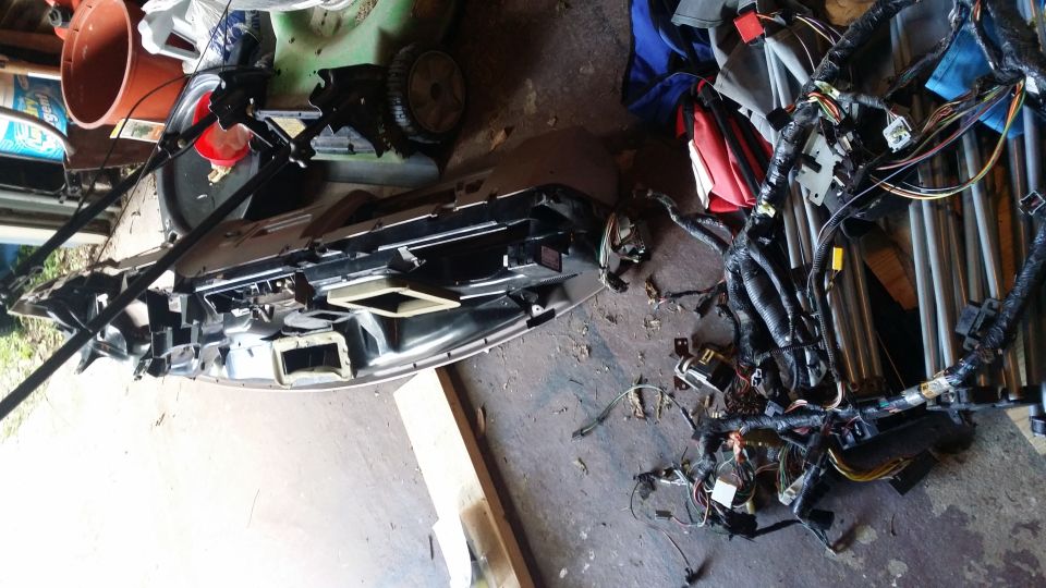 Disassembled car dashboard and wiring harness on a concrete floor.