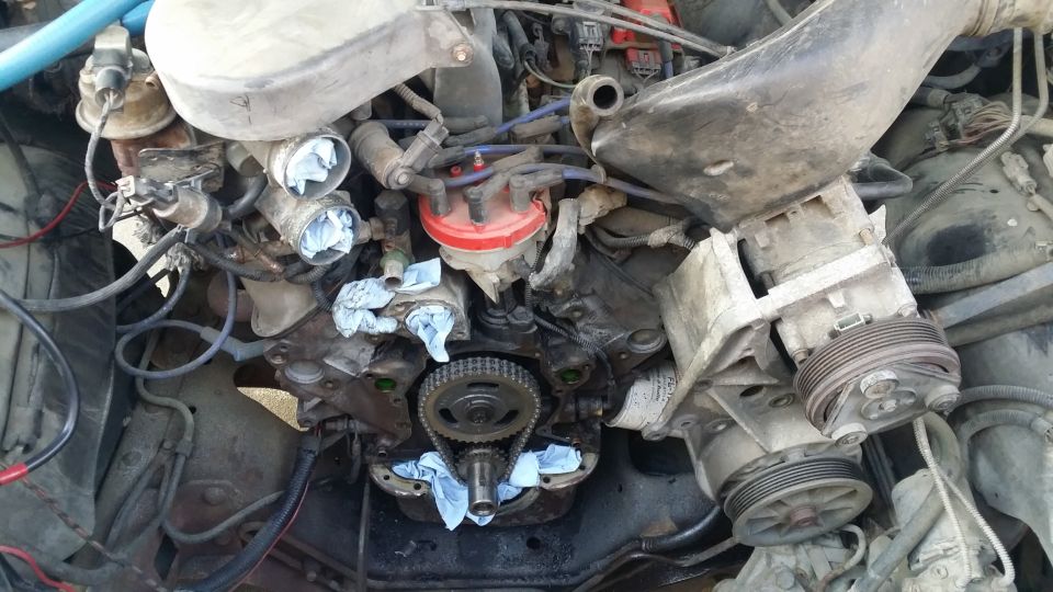 Overhead view of a disassembled V8 engine with timing chain, distributor, and alternator visible.