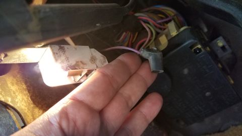 1985 Ford Bronco - A hand holds a disconnected electrical connector with a purple wire near a fuse box and wiring harness under the dashboard of a vehicle.