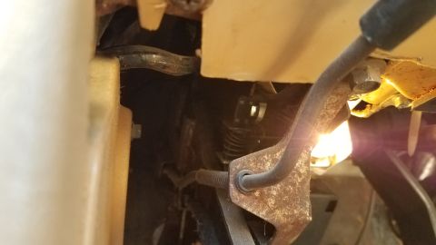 1985 Ford Bronco - A close-up view of a rusty metal lever mechanism with a coiled spring, likely from a vehicle's interior or undercarriage.