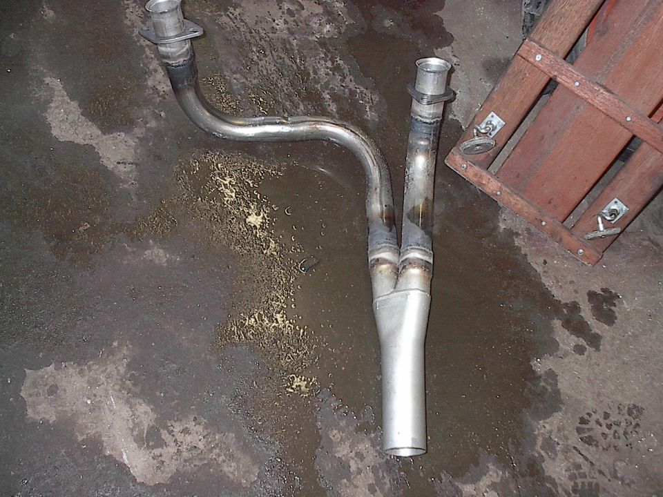 Exhaust Y-pipe with two flanged inlets merging into one outlet, lying on a wet concrete floor