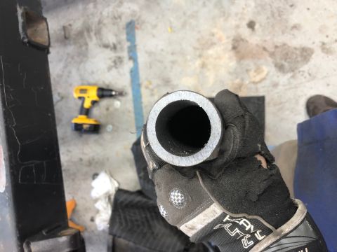 1992 Jeep Wrangler - A gloved hand holds a metal pipe with a cut end, showing the interior. A yellow and black cordless drill is visible on the concrete floor i…