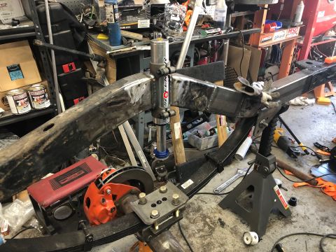 1992 Jeep Wrangler - A close-up view of a modified vehicle frame and suspension components, including leaf springs, a shock absorber, and a brake caliper, in a…
