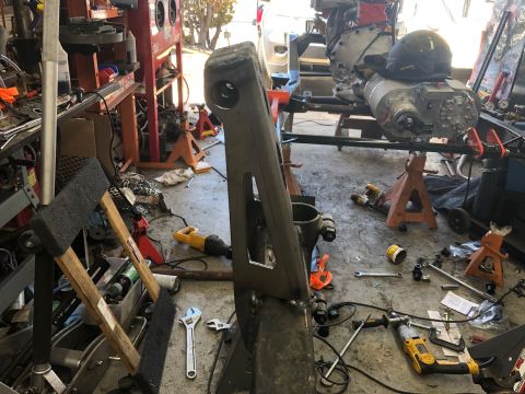 1992 Jeep Wrangler - A workshop scene shows a vehicle's chassis and drivetrain components supported by jack stands. Various tools and parts are scattered on the…