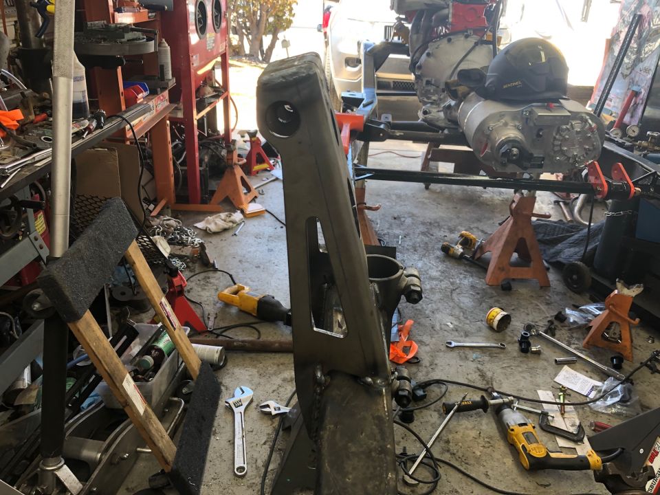 Vehicle chassis and drivetrain components in a workshop with tools on the floor.