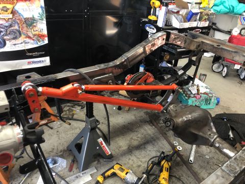 1992 Jeep Wrangler - A custom orange suspension component is mounted to the frame of a Jeep Wrangler, which is supported by jack stands in a garage setting. Too…
