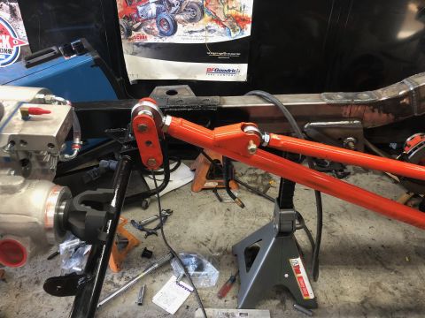 1992 Jeep Wrangler - An orange suspension component is mounted to the frame of a vehicle, which is supported by jack stands in a garage setting. A portion of a…