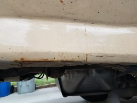1985 Ford Bronco - The underside of a vehicle's body panel shows significant rust along the lower edge, with visible cracks in the paint above. Below the pane…