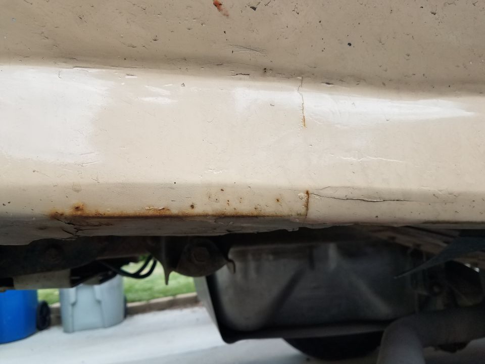 Underside of a vehicle with rust and paint cracks on the body panel.