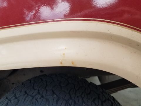 1985 Ford Bronco - A close-up view of the fender flare and wheel well of a vehicle with a two-tone paint scheme. Small spots of rust are visible on the beige…