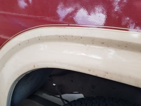 1985 Ford Bronco - Close-up view of the upper rear wheel well area of a vehicle, showing a two-tone paint scheme with a red upper body and a cream-colored fen…