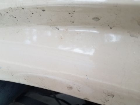 1985 Ford Bronco - A close-up view of the exterior paint on a cream-colored vehicle, showing minor imperfections and chips in the finish.