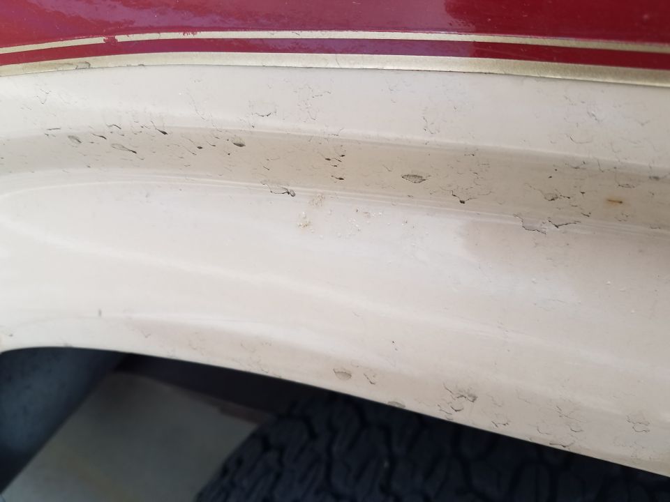 Close-up of peeling paint on a vehicle's lower body panel with red and gold pinstripe.