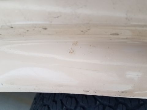 1985 Ford Bronco - A close-up view of the lower body panel of a light-colored vehicle, showing chipped paint and some dirt. The tread of a tire is visible at…