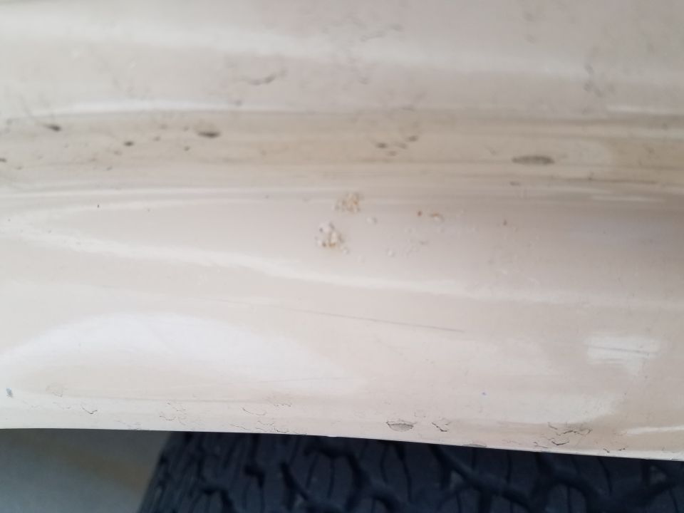 Close-up of chipped paint on a light-colored vehicle body panel above a tire.
