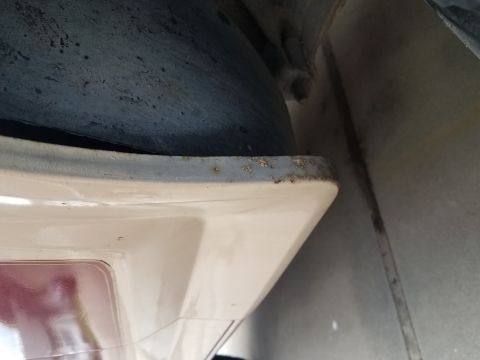 1985 Ford Bronco - A close-up view shows the edge of a cream-colored body panel, possibly a fender flare or bumper, with visible rust spots along its upper me…