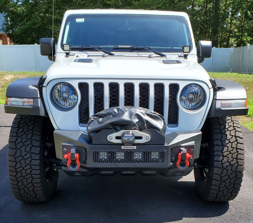 White Jeep Wrangler front view with aftermarket bumper, winch, and red tow hooks.