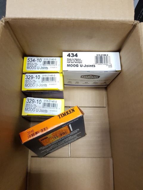 1978 Ford Bronco - A cardboard box filled with various automotive parts, including several Moog U-Joints and a Timken part. The box is open and viewed from a…
