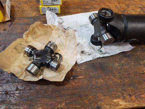 1978 Ford Bronco - A new U-joint is shown on brown paper next to a driveshaft with a U-joint attached, resting on a white paper towel on a wooden workbench. T…