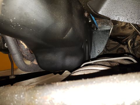 1978 Ford Bronco - A low-angle view of the underside of a vehicle, showing the black oil pan, exhaust manifold, and part of the frame. The scene appears to be…
