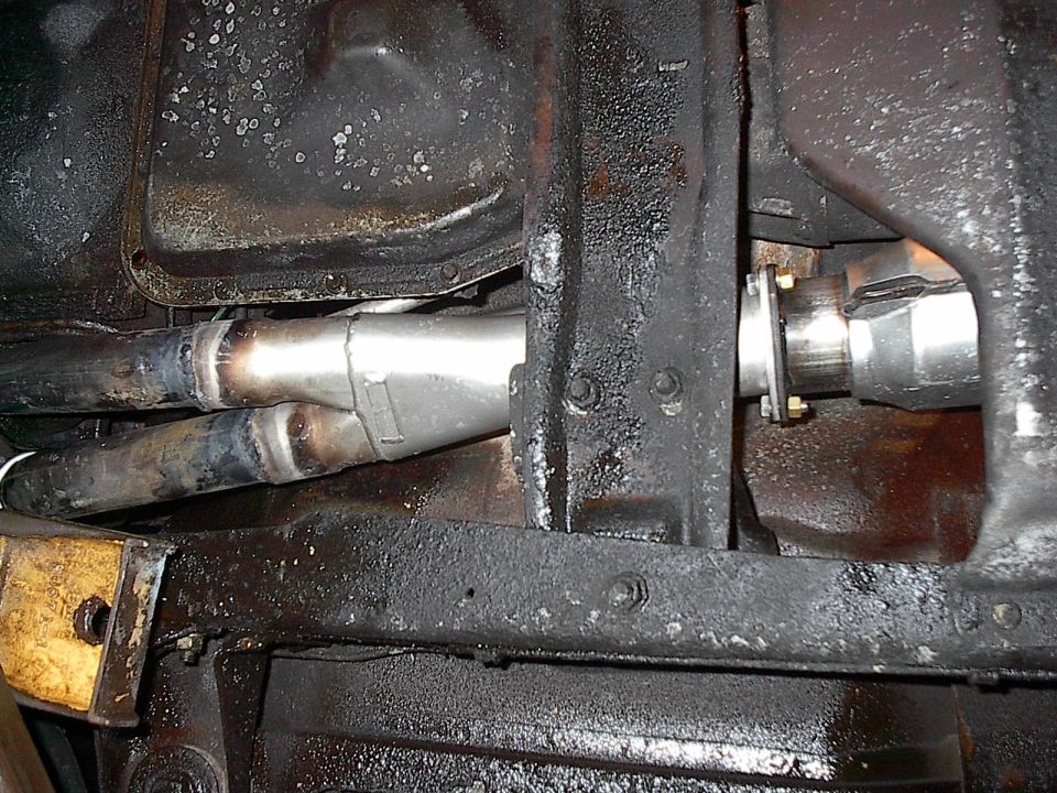 Underside view of new exhaust Y-pipe and flange connection beneath a black-coated frame and floor pan