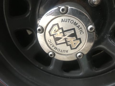 1994 Ford Bronco - A close-up of a chrome automatic 4x4 hubcap on a dark-colored vehicle wheel. The hubcap has the text "AUTOMATIC 4x4" in a circular pattern.