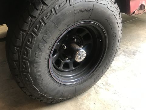 1994 Ford Bronco - A close-up of a black Ironman All Country A/T tire mounted on a black steel wheel. The tire has white lettering and is attached to a vehicl…