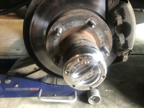 1994 Ford Bronco - A close-up view of a vehicle's front wheel hub assembly, featuring a chrome hubcap with "MI" and "LOCK" and "FREE" text, is supported by a…