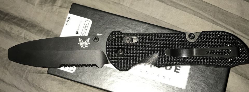 Black Benchmade folding knife with serrated edge on a black box.