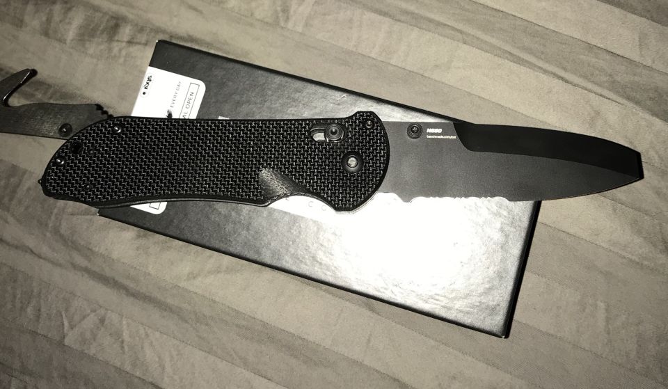 Black folding knife with seatbelt cutter on textured handle, resting on a black box.