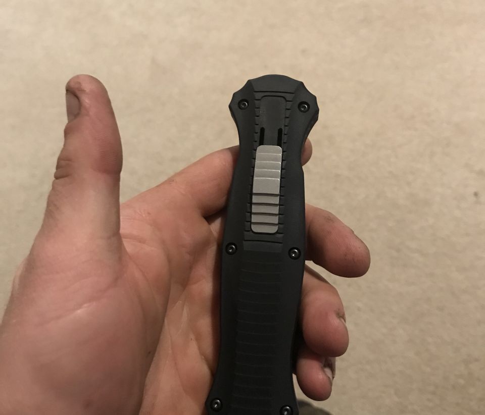 Hand holding a black automatic knife with a silver slider
