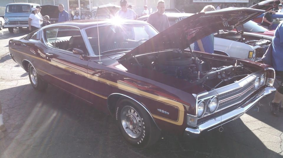 Maroon 1970 Ford Torino GT with gold stripes, hood open, parked outdoors.