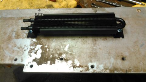 1978 Ford Bronco - A black oil cooler with two inlet/outlet ports is mounted on a metal surface. Text written in black marker above the cooler reads "FRT" wit…