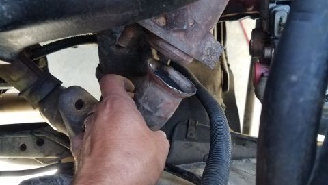 1985 Ford Bronco - A hand is holding a rusted exhaust pipe fitting that appears to be broken off from a vehicle's exhaust system. The fitting is metallic and…