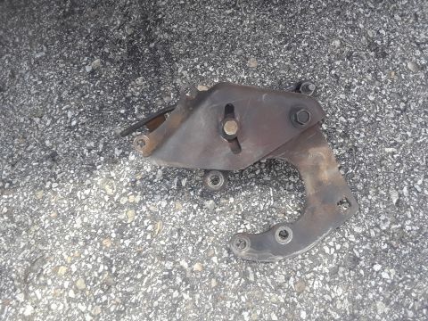 1994 Ford Bronco - A rusty metal bracket with bolts is lying on a gravel surface. The bracket appears to be a vehicle part, possibly from the engine bay or su…