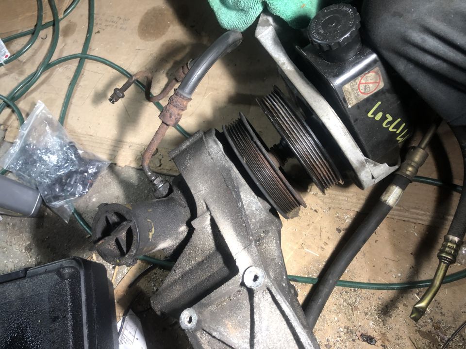 Disassembled power steering pump, reservoir, and hoses on a concrete floor.