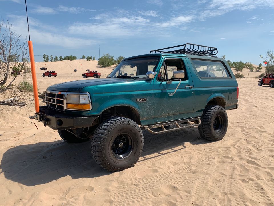 Teal Ford Bronco with roof rack and aftermarket bumper on sand dunes