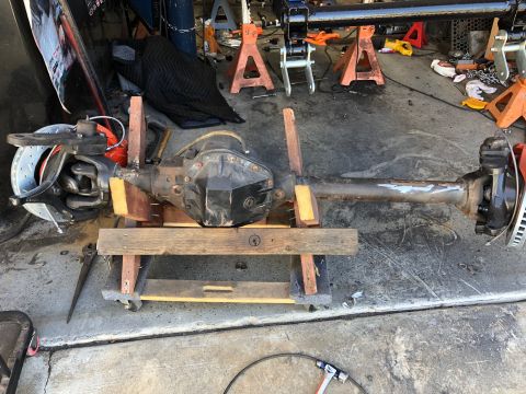 1992 Jeep Wrangler - A vehicle's front axle assembly, including the differential, brake rotors, and suspension components, is mounted on a wooden stand in a gar…
