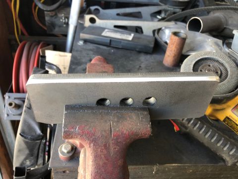 1992 Jeep Wrangler - A close-up view of a metal blade with three holes, clamped in a vise. The blade has a sharpened edge with a white line indicating the bevel.