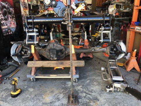 1992 Jeep Wrangler - A front axle assembly, likely from a Jeep Wrangler, is supported by jack stands and a rolling cart in a garage setting. The axle features d…