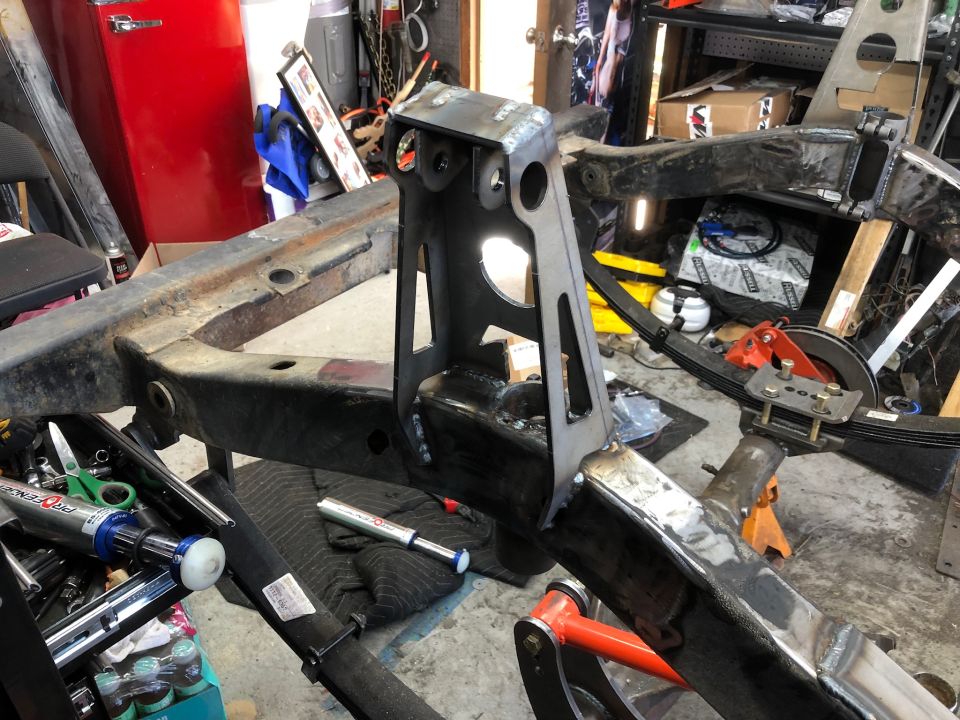 Jeep Wrangler frame with welded modifications and leaf spring suspension in a workshop.