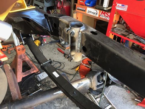 1992 Jeep Wrangler - A black Jeep Wrangler frame is supported by jack stands in a garage. Various tools and parts are scattered around the vehicle.