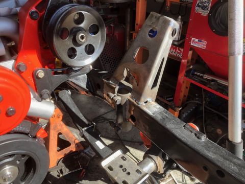 1992 Jeep Wrangler - A close-up view of a vehicle's engine bay and frame, showing a power steering pump assembly mounted to a red bracket, and a section of the…