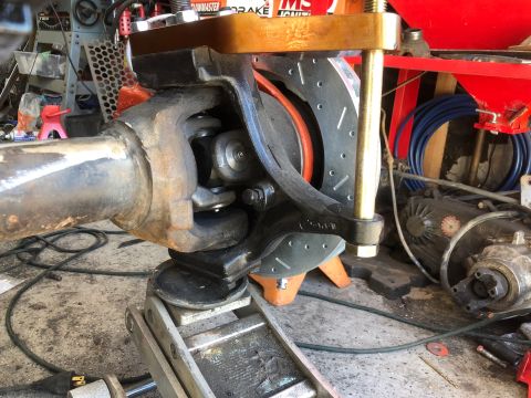 1992 Jeep Wrangler - A close-up view of a vehicle's front axle assembly, featuring a u-joint, brake rotor, and caliper, supported by a hydraulic jack. The scene…