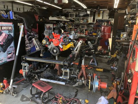 1992 Jeep Wrangler - Disassembled Jeep Wrangler chassis and engine in a garage, with various tools and parts scattered around.