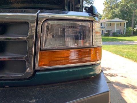 1996 Ford Bronco - Close-up of a green Ford truck's front grille and headlight assembly, with the hood open.