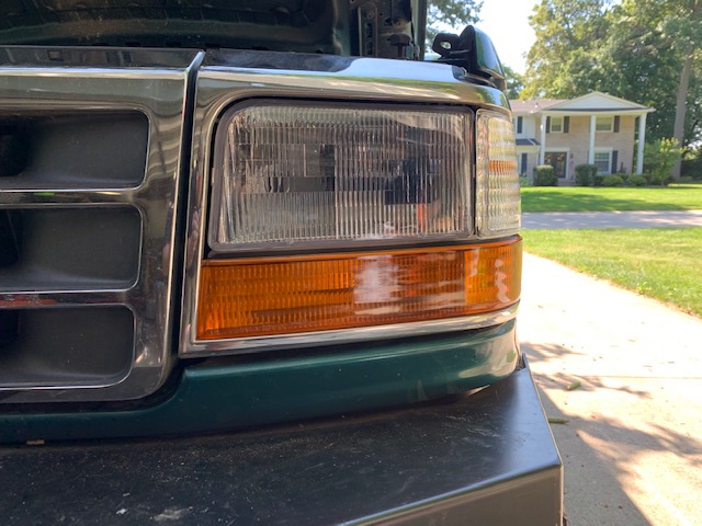 Green Ford truck front end with chrome grille and amber turn signals. Hood is up. House in background