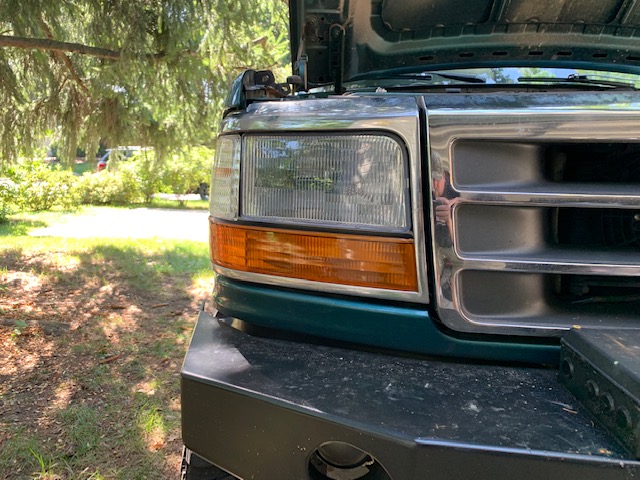 Green Ford truck front end with hood open, showing chrome grille and headlight