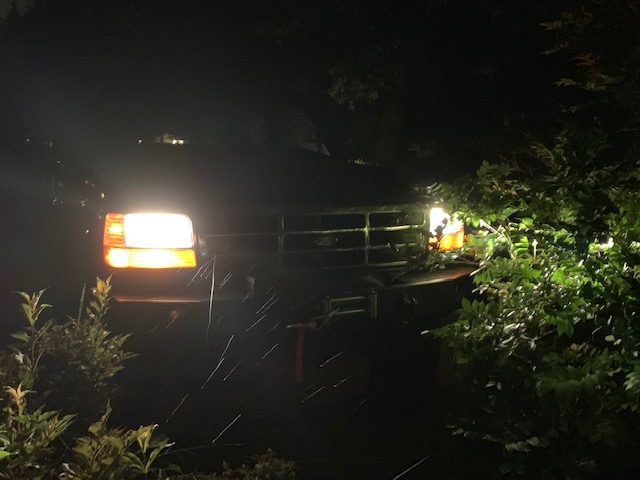 1996 Ford Bronco front view at night, headlights on, surrounded by trees.
